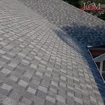 A high-angle view of a grey architectural asphalt shingle roof with a prominent seam and a glimpse of a nearby structure.