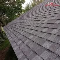 A low-angle view of a grey architectural asphalt shingle roof on a sunny day with trees in the background.