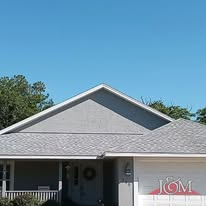 A light gray house exterior with a gabled roof, an attached garage, and surrounding green trees under a clear blue sky.