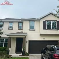 A two-story, cream-colored house with a dark brown garage door and a dark-framed entryway, under a cloudy sky.
