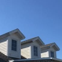 Three cream-colored house dormers with dark windows and gabled roofs sit against a clear blue sky.