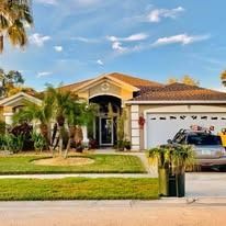 A one-story suburban home with a two-car garage, palm trees in the front yard, and a car parked in the driveway.