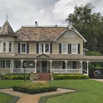 A two-story Victorian-style house with a wraparound porch, a turret, and a lawn in the foreground.
