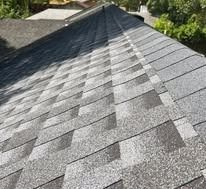 A close-up view of a shingled roof with a diagonal transition between weathered dark shingles and newer, lighter ones.