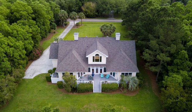 Aerial view of a house with a gray roof and white siding, surrounded by a lush green lawn and dense forest.