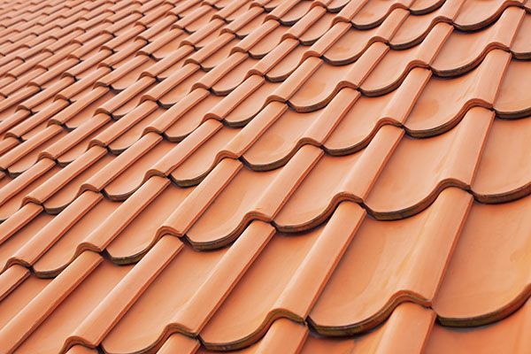 An angled close-up of terracotta-colored, S-shaped clay roof tiles arranged in a repeating pattern.