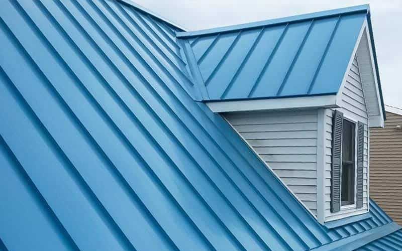 A bright blue standing-seam metal roof with a gabled dormer window featuring white siding and grey shutters.