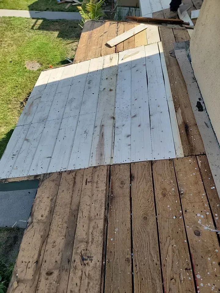 Wooden deck being repaired with new white boards on top of weathered brown boards.