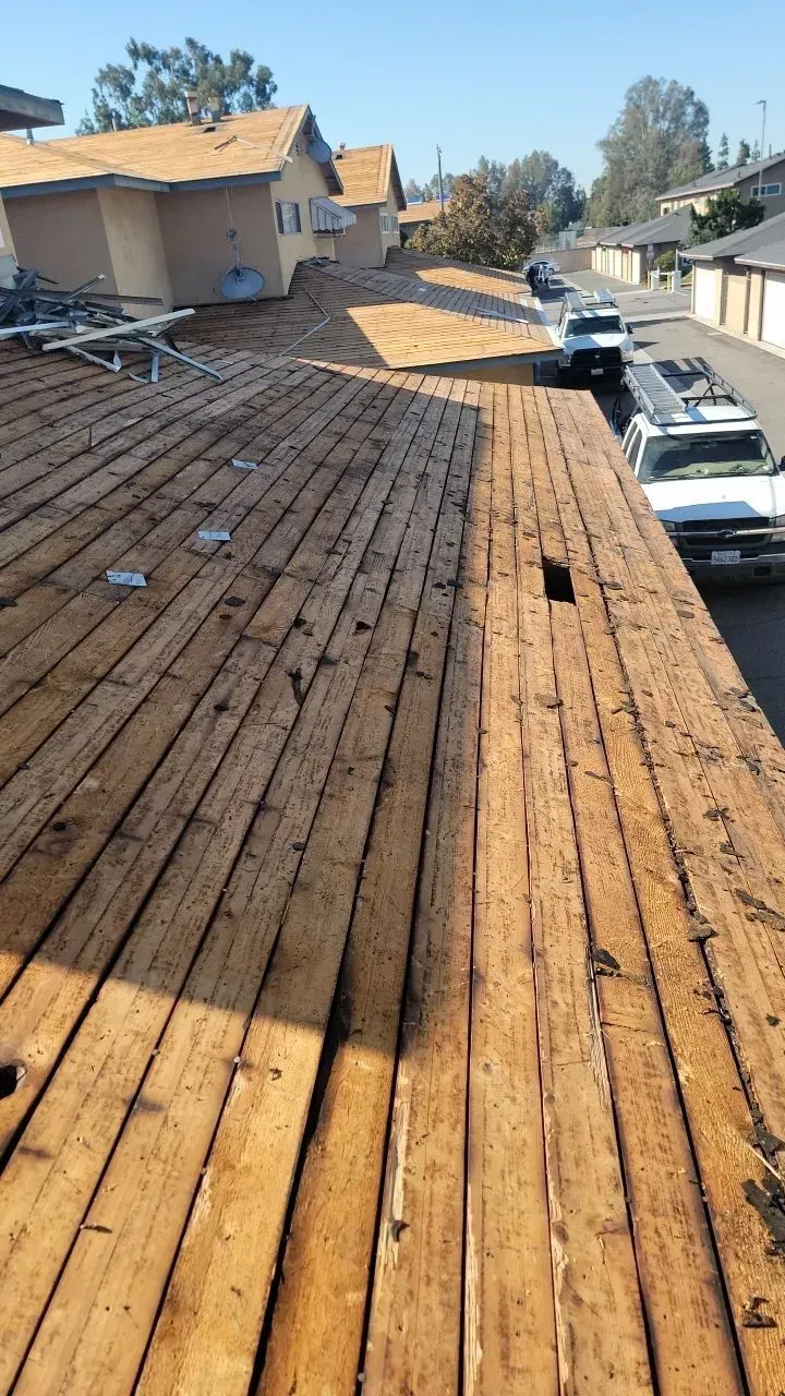 Wooden planks on a roof, construction site. Buildings, parked trucks, clear sunny day.