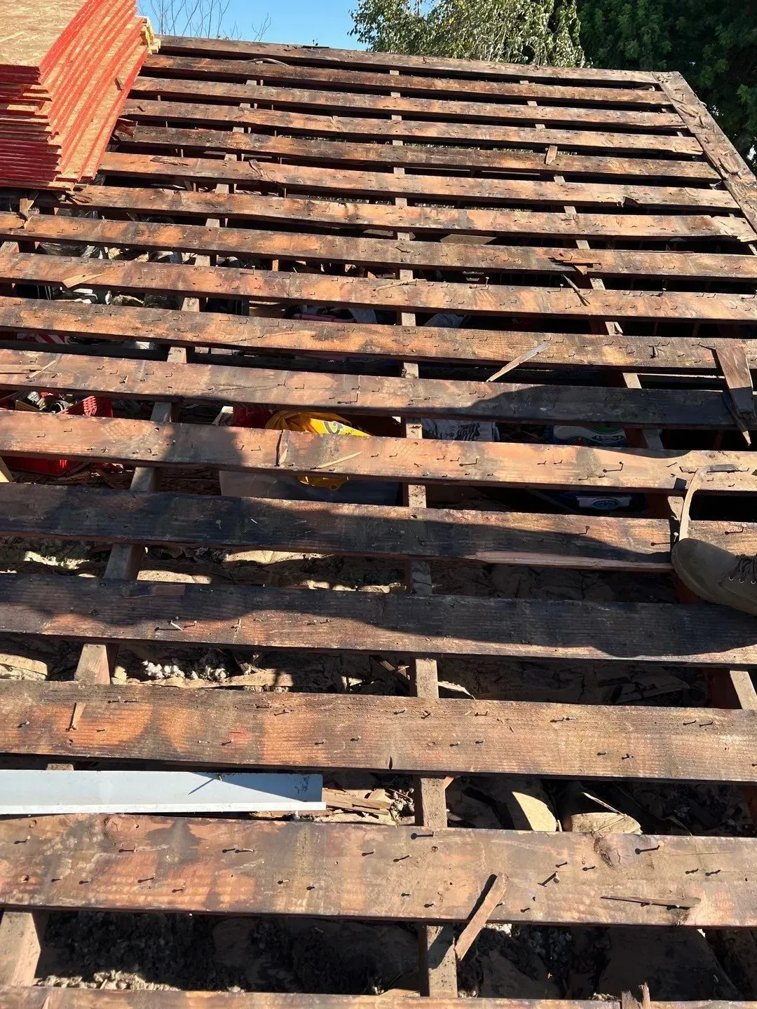 Rooftop with exposed wooden beams, missing tiles, and a stack of new tiles.