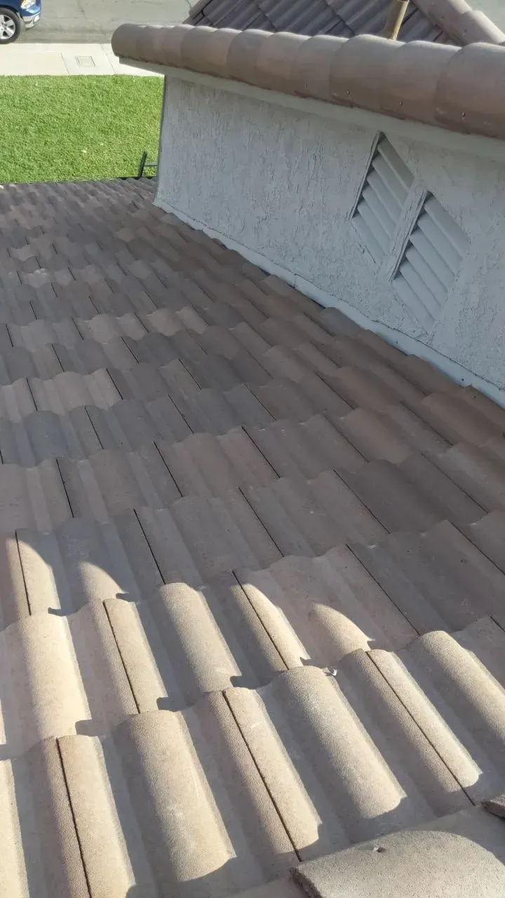 Tan tile roof next to a stucco wall with a geometric vent, sunny outdoor setting.