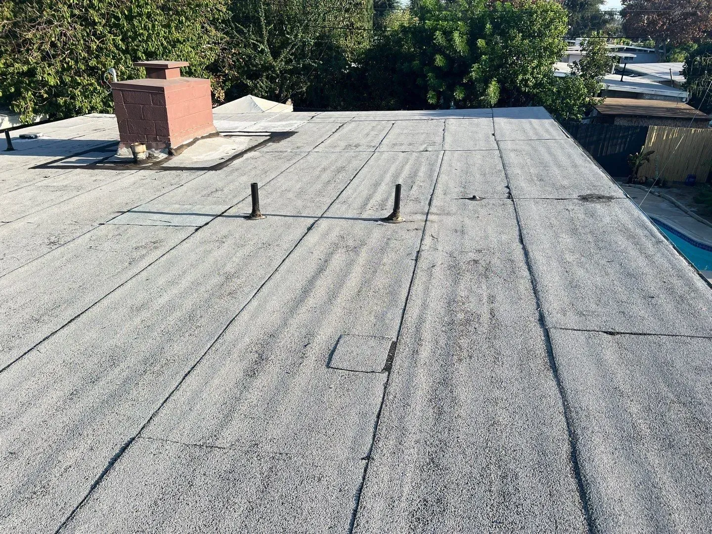 Flat, gray rooftop with a chimney, vents, and visible seams.