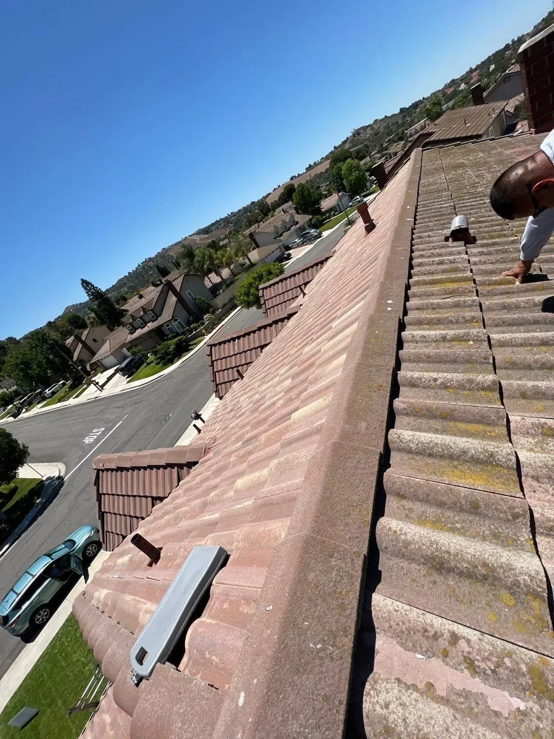 Person on tile roof, sunny day. Residential setting, brown tiles, blue sky.
