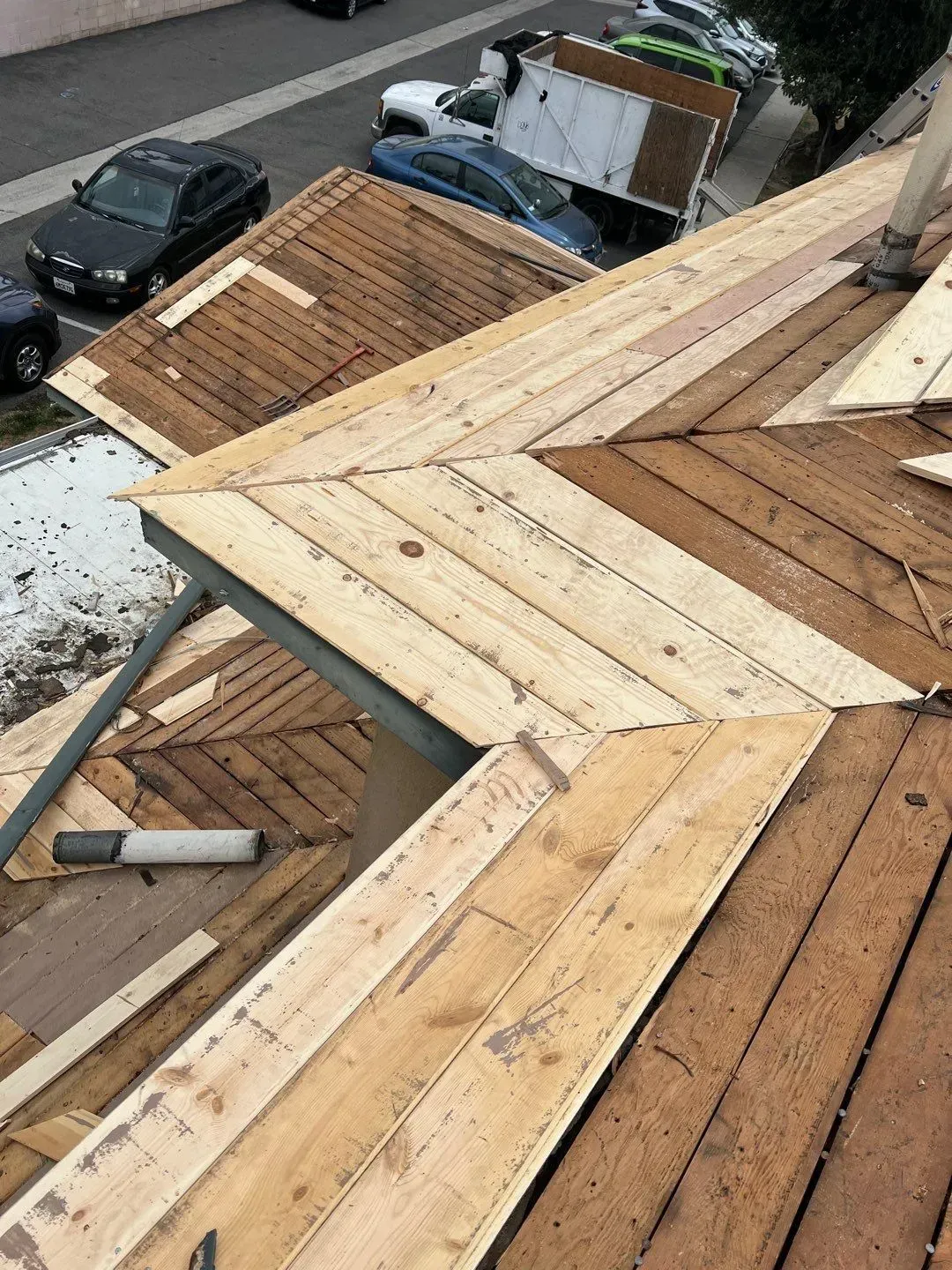 Construction worker on roof, replacing wooden shingles. Cars parked below.