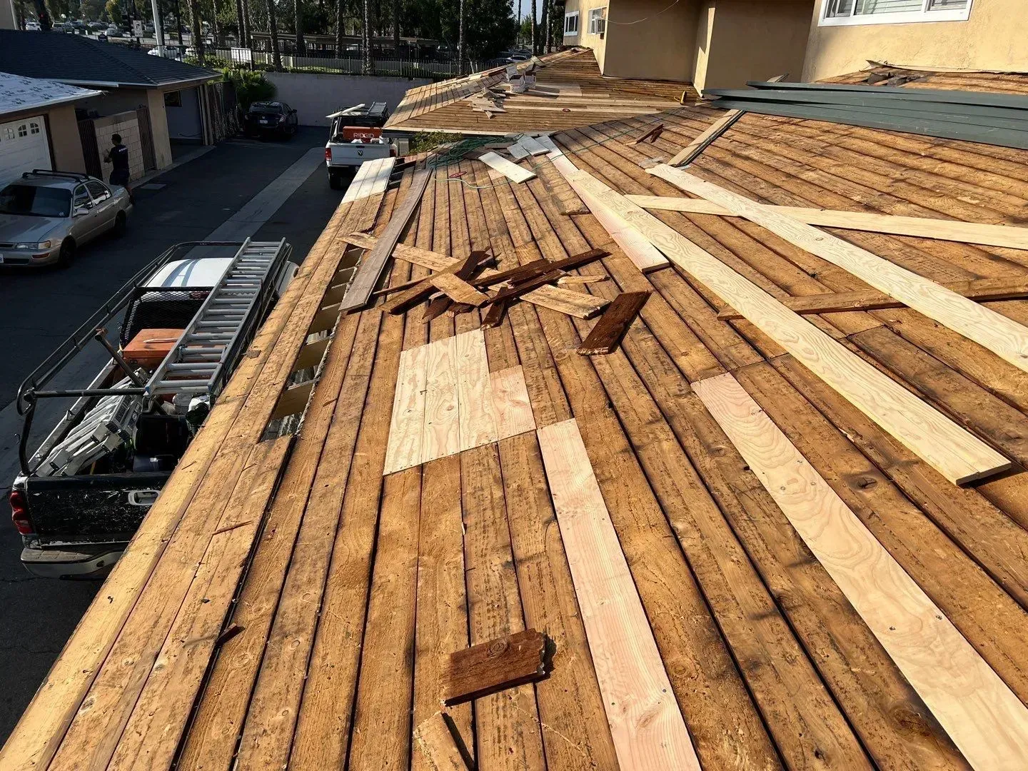 Roofing work on a house; planks and debris on the roof, truck with ladder parked beside a building.
