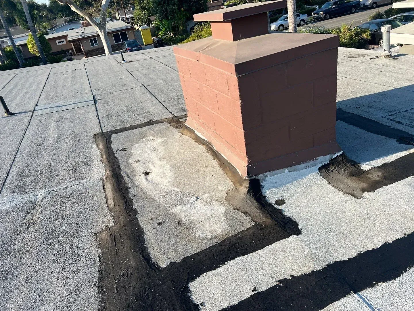 Flat roof with a brown chimney; black sealant borders the chimney base on the weathered surface.
