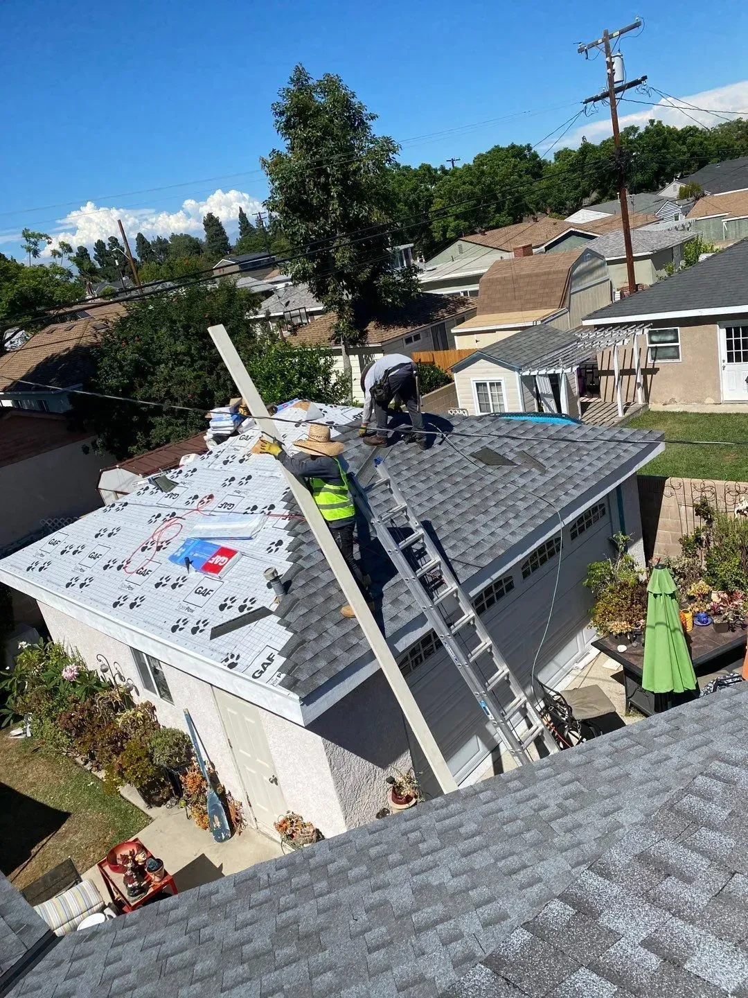 Roofers installing new shingles on a residential roof on a sunny day.