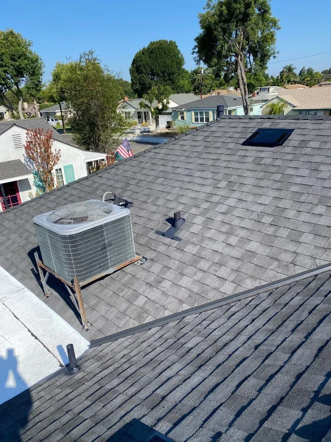 Dark gray shingle roof with AC unit, skylight, and vent; residential neighborhood.