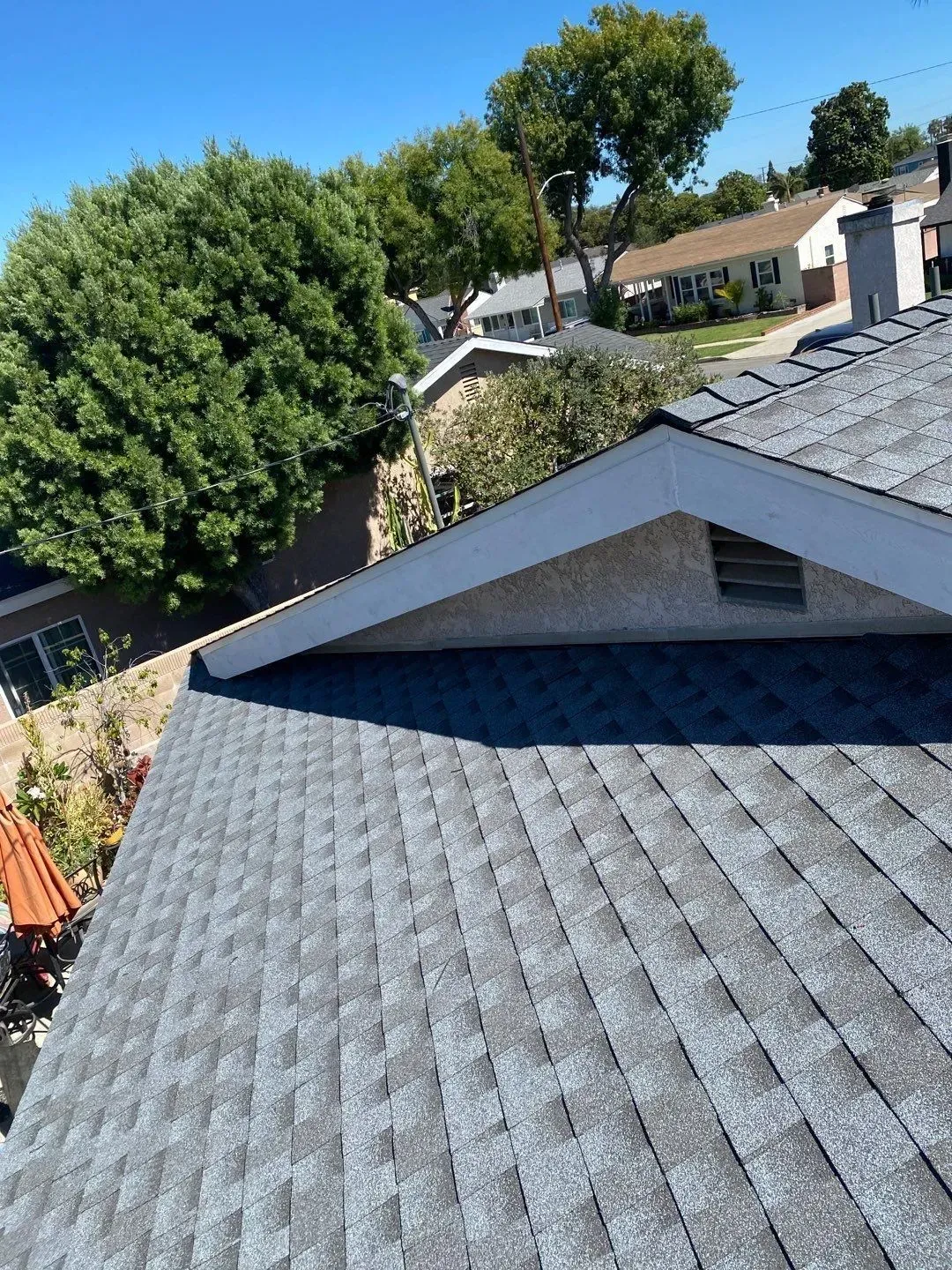 Gray asphalt shingle roof on a house, with a blue sky and green trees in the background.