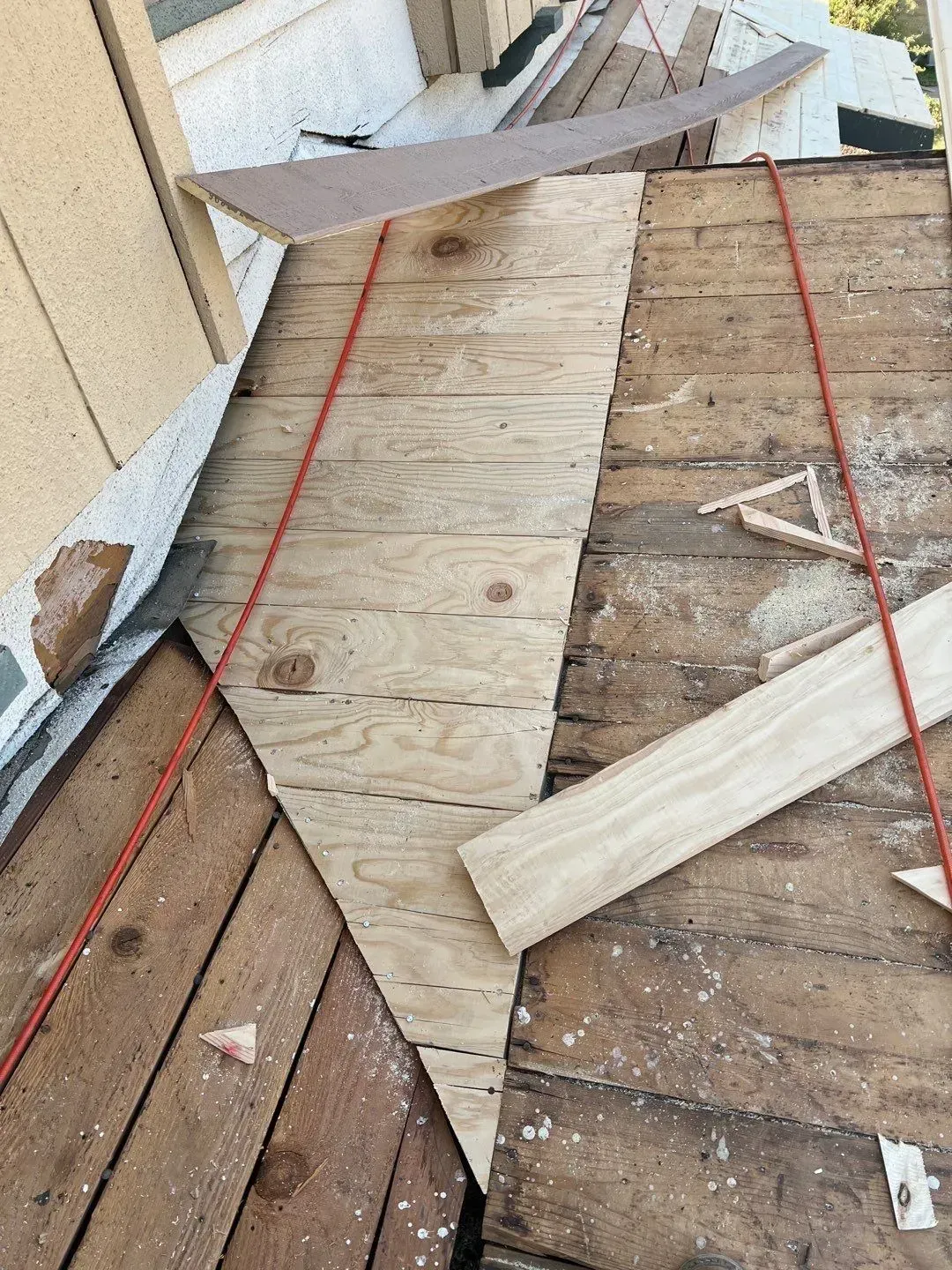 Rooftop with exposed plywood and wood slats being repaired; a red rope runs across the surface.