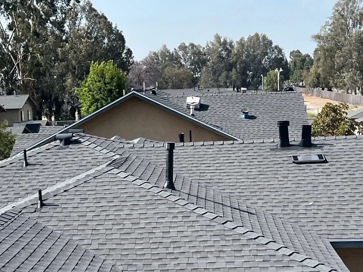 Gray shingle roofs of homes with vents, set against trees and blue sky.