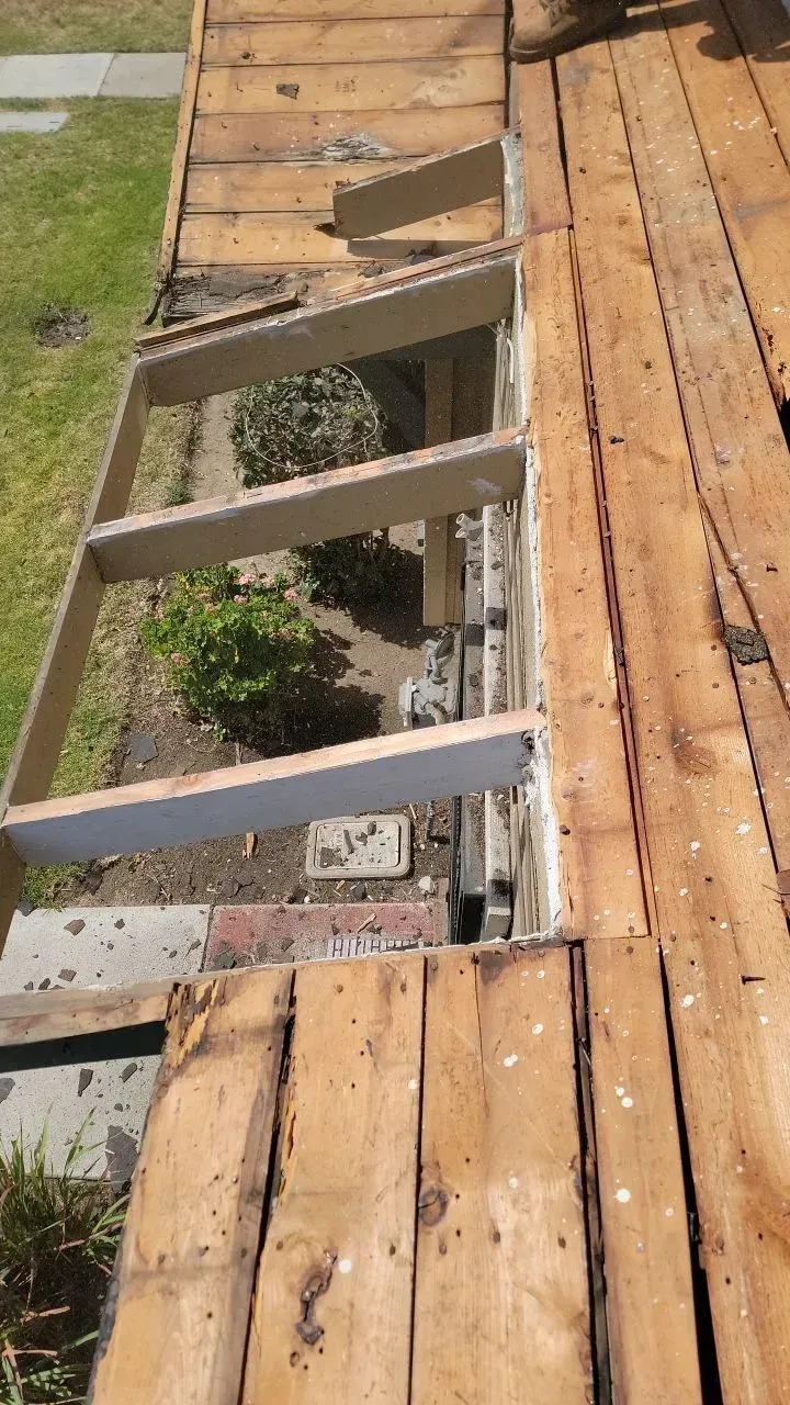 Partially dismantled wooden deck with a framed opening, revealing the ground below.