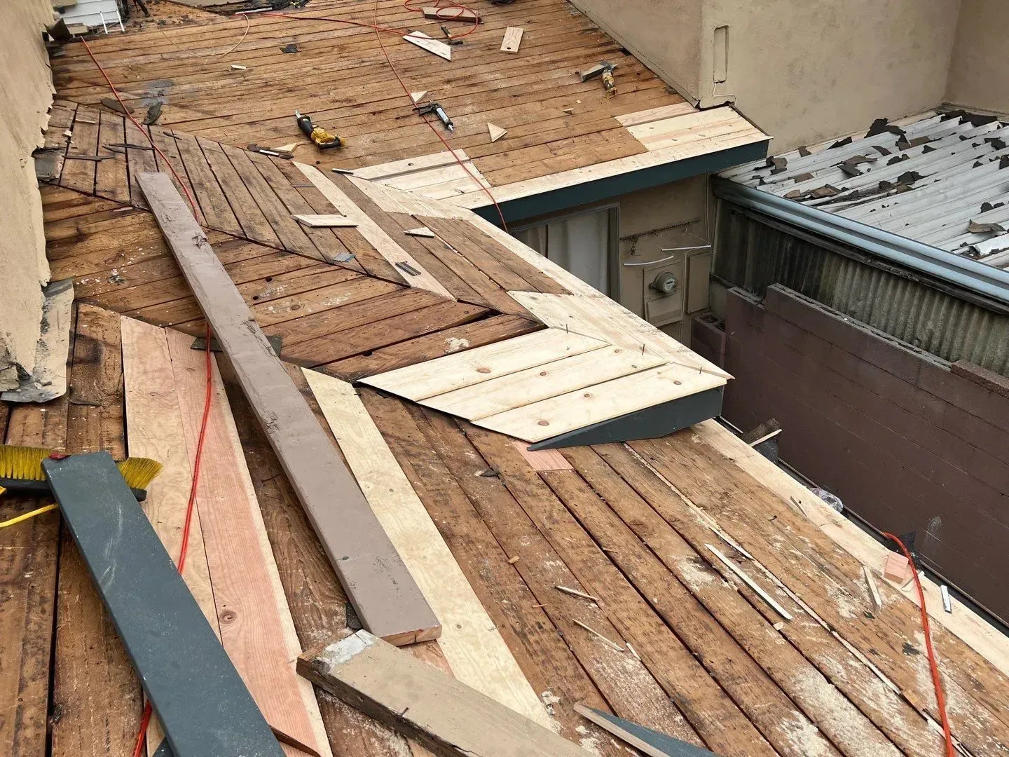 Rooftop undergoing repairs; exposed wooden boards and new planks scattered across the surface.