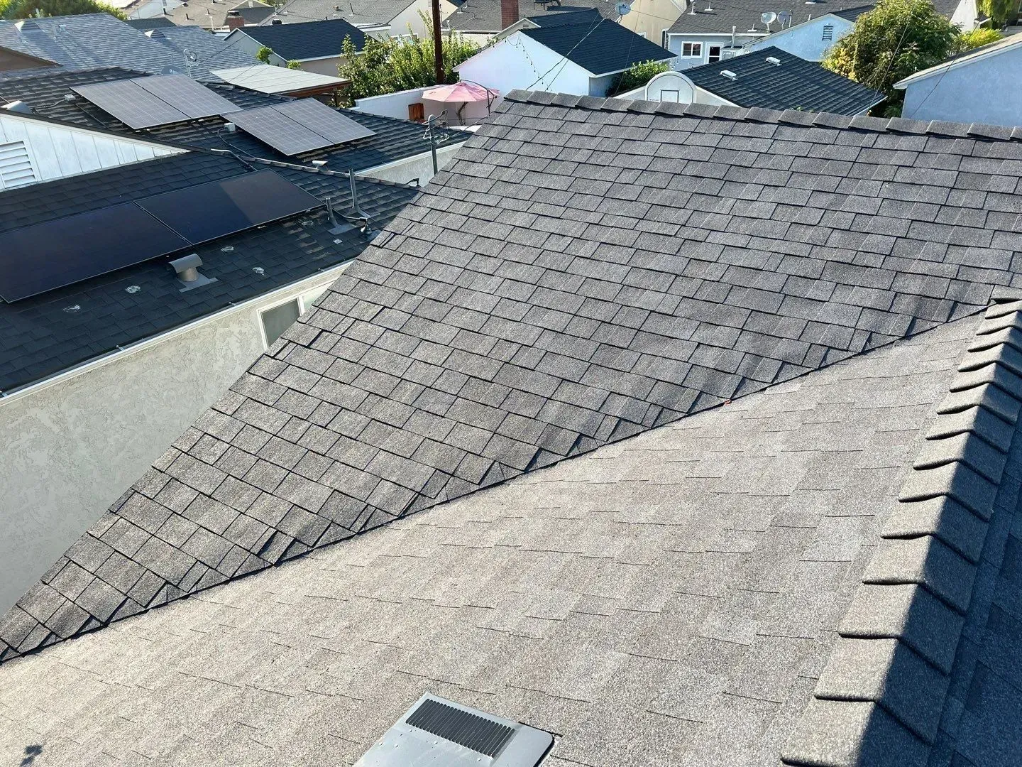 Overhead view of gray asphalt shingle roofs in a residential neighborhood, some with solar panels.