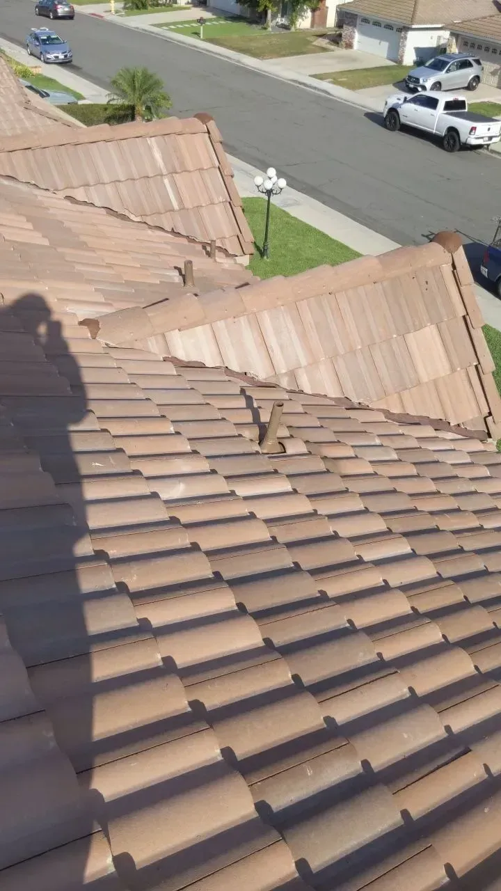 Brown tile roof with sunlight, overlooking a residential street with cars and green lawns.