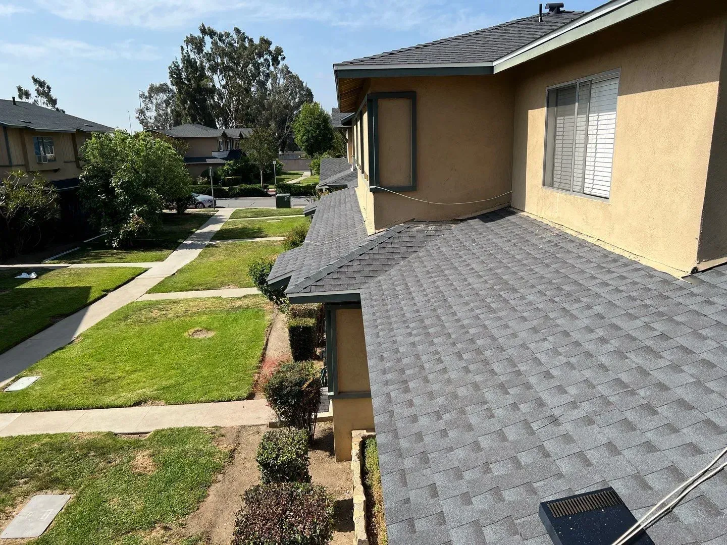 Residential building with a dark gray shingle roof, green lawn, and trees.