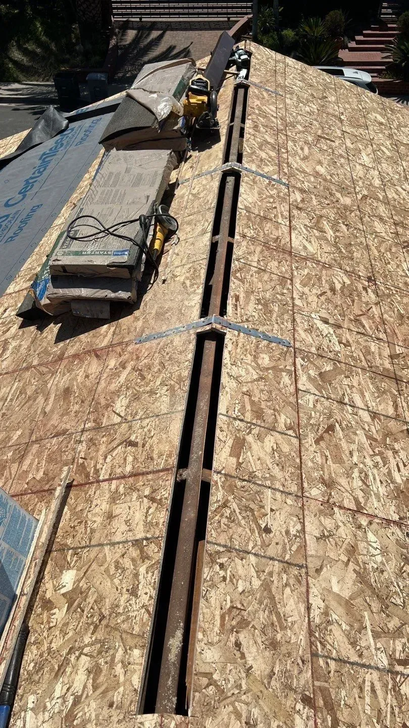 Rooftop with central vent; plywood, construction equipment, and materials; sunny day.