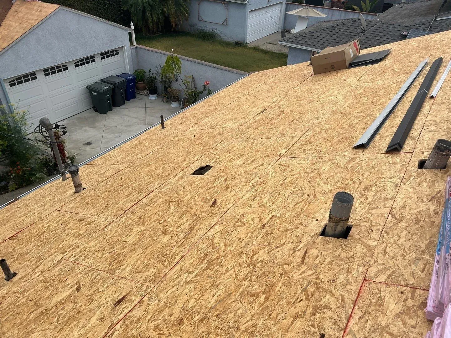 Rooftop with exposed wood sheathing, near a garage and houses.