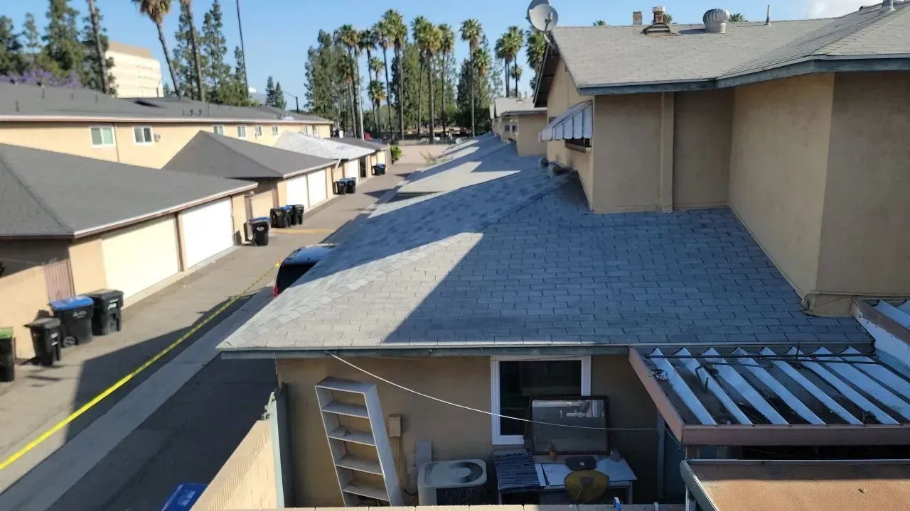 View of apartment complex with beige buildings, gray roofs, and palm trees in the background.