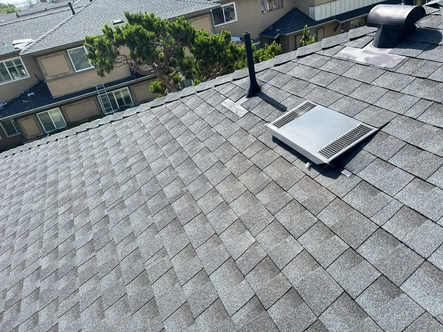 Gray asphalt shingle roof with a vent and chimney against a residential building.