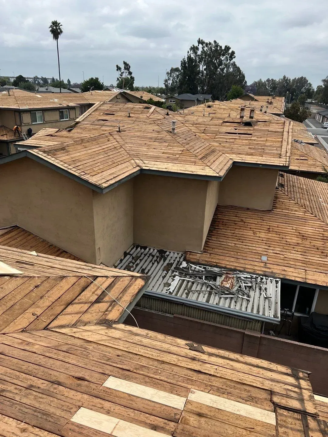 Roofs of multiple buildings during roof repair, some brown shingles missing. Overcast day.