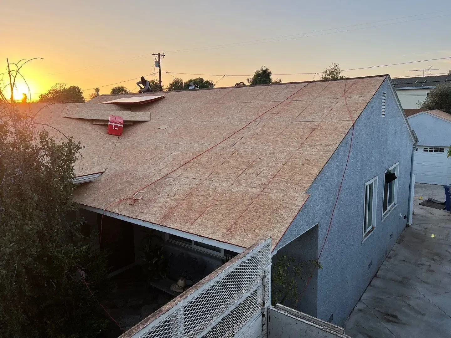 House roof partially covered with new plywood, sunset in background.