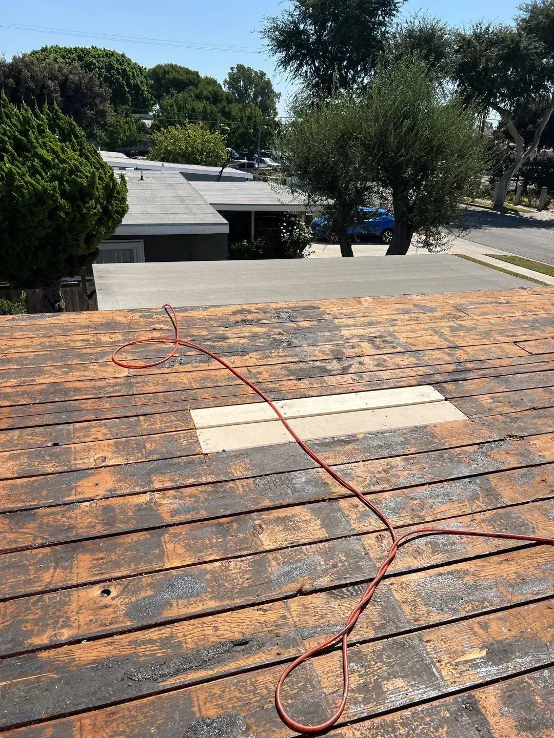 Rusted roof with a patch, red wire, and a residential neighborhood in the background on a sunny day.