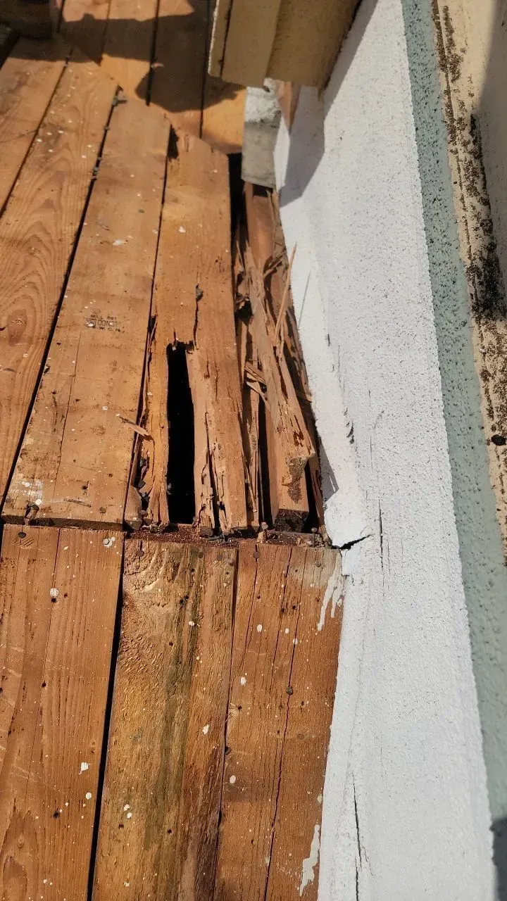 Decayed wooden planks beside a white wall with a split, likely due to water damage or rot.