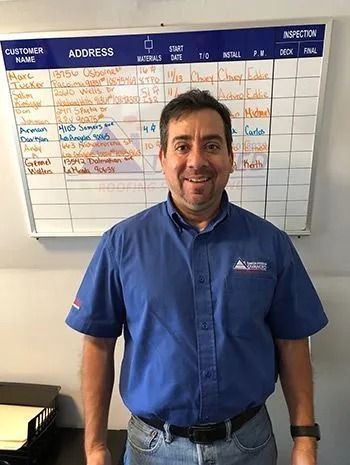 Man in blue shirt stands in front of a whiteboard with customer information, smiling.