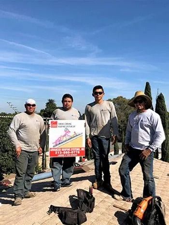 Four roofers on a rooftop holding a sign; sunny day.