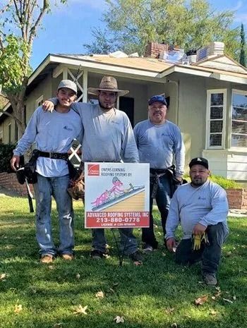 Four roofers pose with a sign in front of a house with a partially replaced roof.