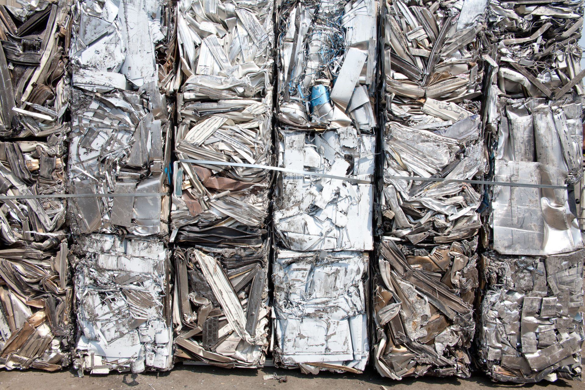 Stacked bundles of crushed metal scrap wrapped in white wire, with a blue item among them