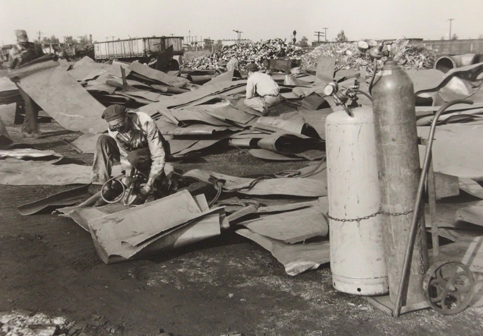 Destroyed aircraft wreckage scattered across a field, with two upright gas cylinders in the foreground.