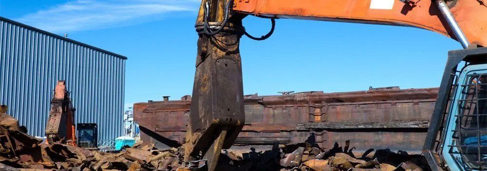 Excavator demolishing debris near a blue shipping container at a construction site under a clear sky