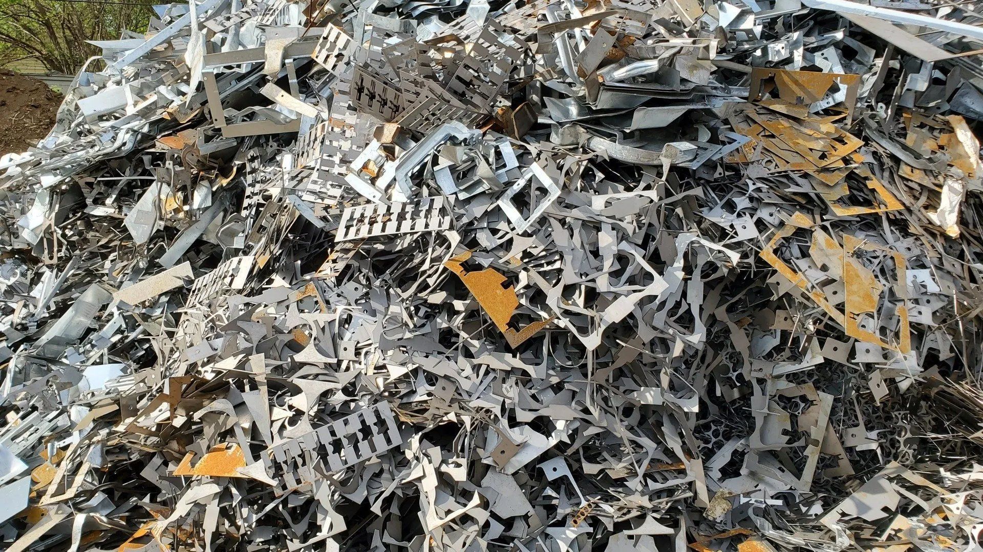 Heap of mixed scrap metal debris, mostly gray with some yellow pieces, piled outdoors.
