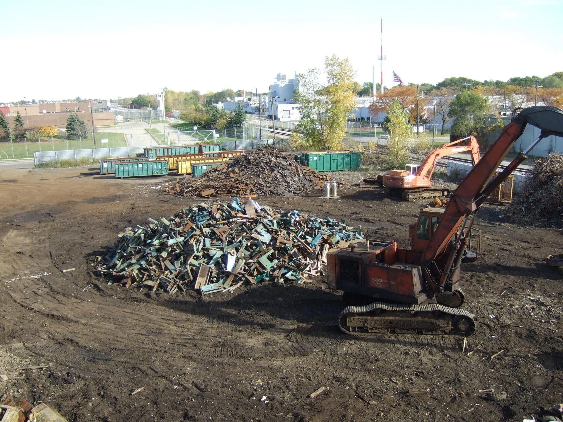 Excavator at a scrapyard beside piles of crushed cars and metal debris