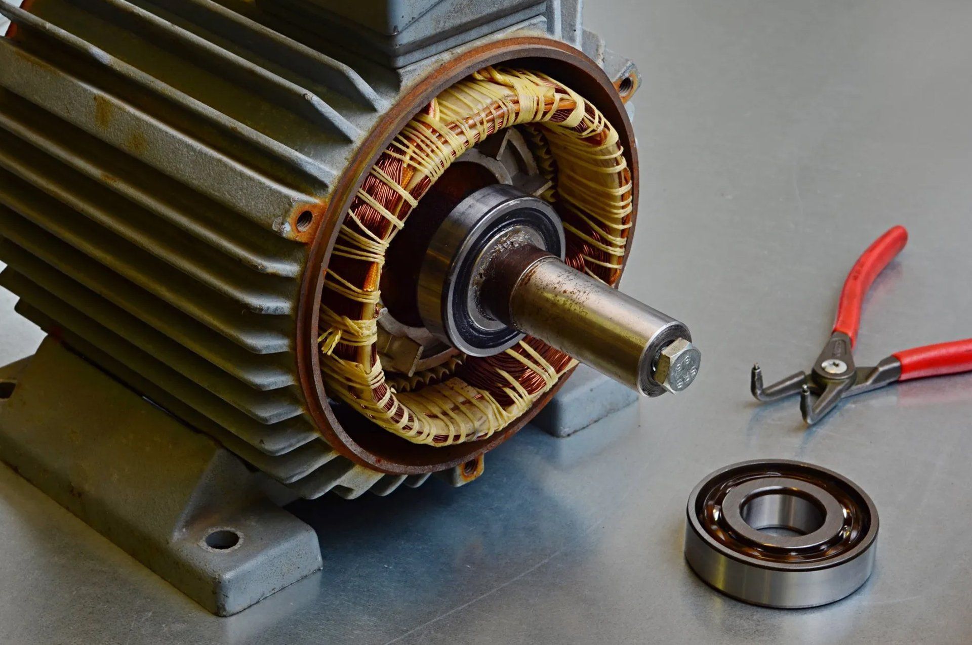 Partially disassembled electric motor with pliers and a bearing on a gray work surface