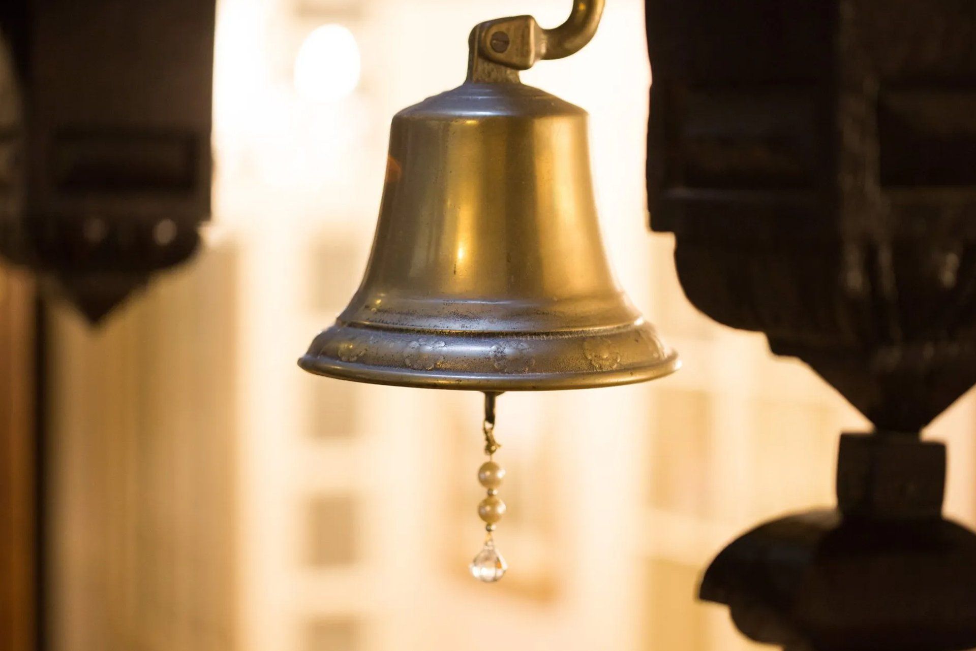 Brass bell with a clapper hanging in a softly lit interior.
