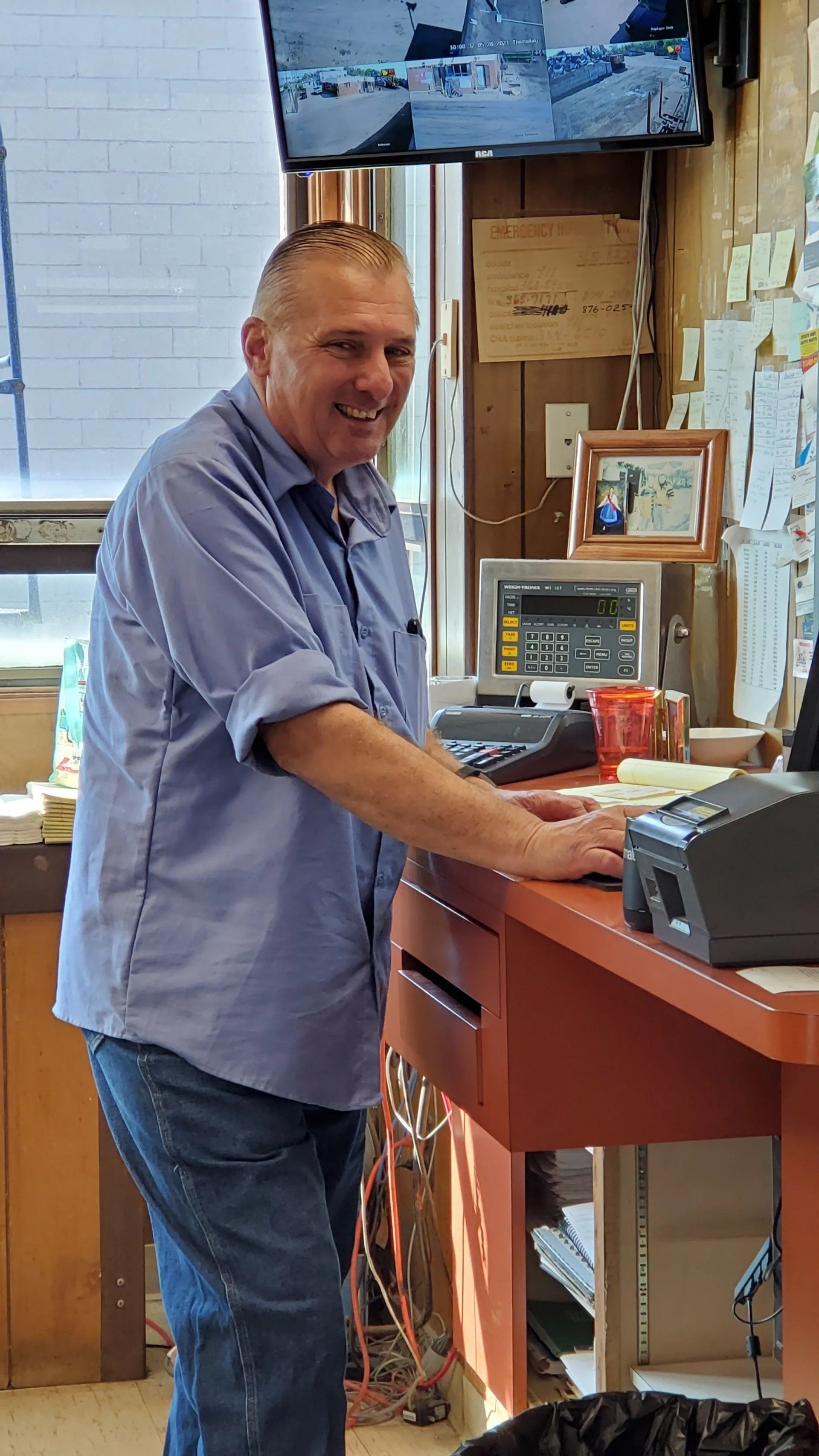 Man in blue shirt smiling at a workbench in a shop, with tools and a monitor nearby