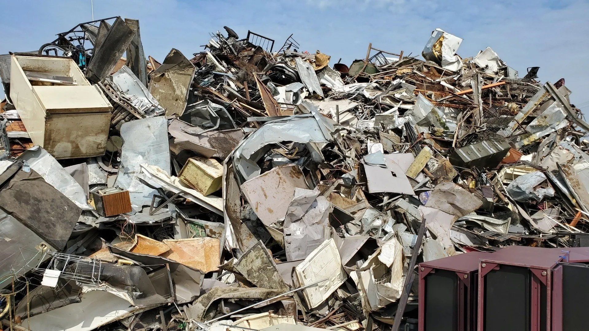 Pile of twisted scrap metal and rubble at a demolition or junkyard site under a clear blue sky.